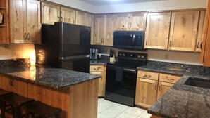 A kitchen with wooden cabinets, a black refrigerator, a microwave, a stove, and bar stools. - Sweet Retreat Cozy Cabin (Sisters)