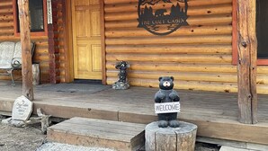 A wooden cabin with a 'Welcome' sign and a bear statue holding a 'Welcome' sign. - Sweet Retreat Cozy Cabin (Sisters)