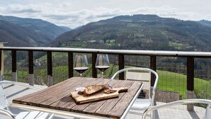 Ett träbord med två vinglas och en skärbräda med bröd, placerat på en balkong med utsikt över bergen.