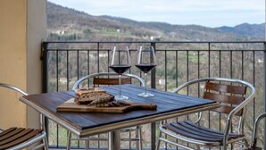 Un balcón con una mesa dispuesta para dos personas, con pan y copas de vino, con vistas a un paisaje montañoso.