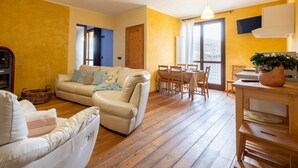 Una sala de estar acogedora con un sofá, una mesa de comedor con sillas, piso de madera y un amplio ventanal con cortinas.