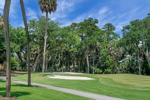 A golf course with a well-maintained fairway, sand bunkers, and a clear sky.
