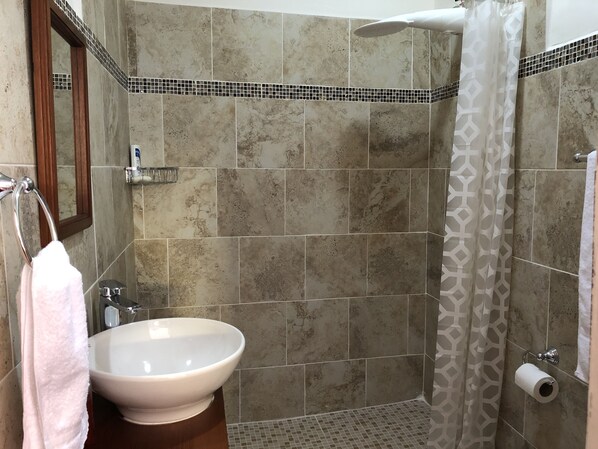 A bathroom with a sink, mirror, shower, and tiled walls.