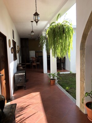 A covered patio area with terracotta tiles, hanging plants, and a dining area with wooden furniture.