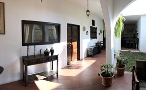 Un pasillo iluminado por el sol con una consola de madera, plantas en macetas y vistas a un comedor.