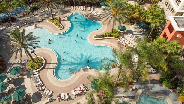 An aerial view of a resort with a large, winding pool surrounded by palm trees and sun loungers. - Vacation Village at Parkway, Kissimmee, FL (Kissimmee)