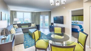 A modern living room with a sofa, a glass coffee table, and chairs. There is a television mounted on the wall and a balcony with curtains. - Vacation Village at Parkway, Kissimmee, FL (Kissimmee)