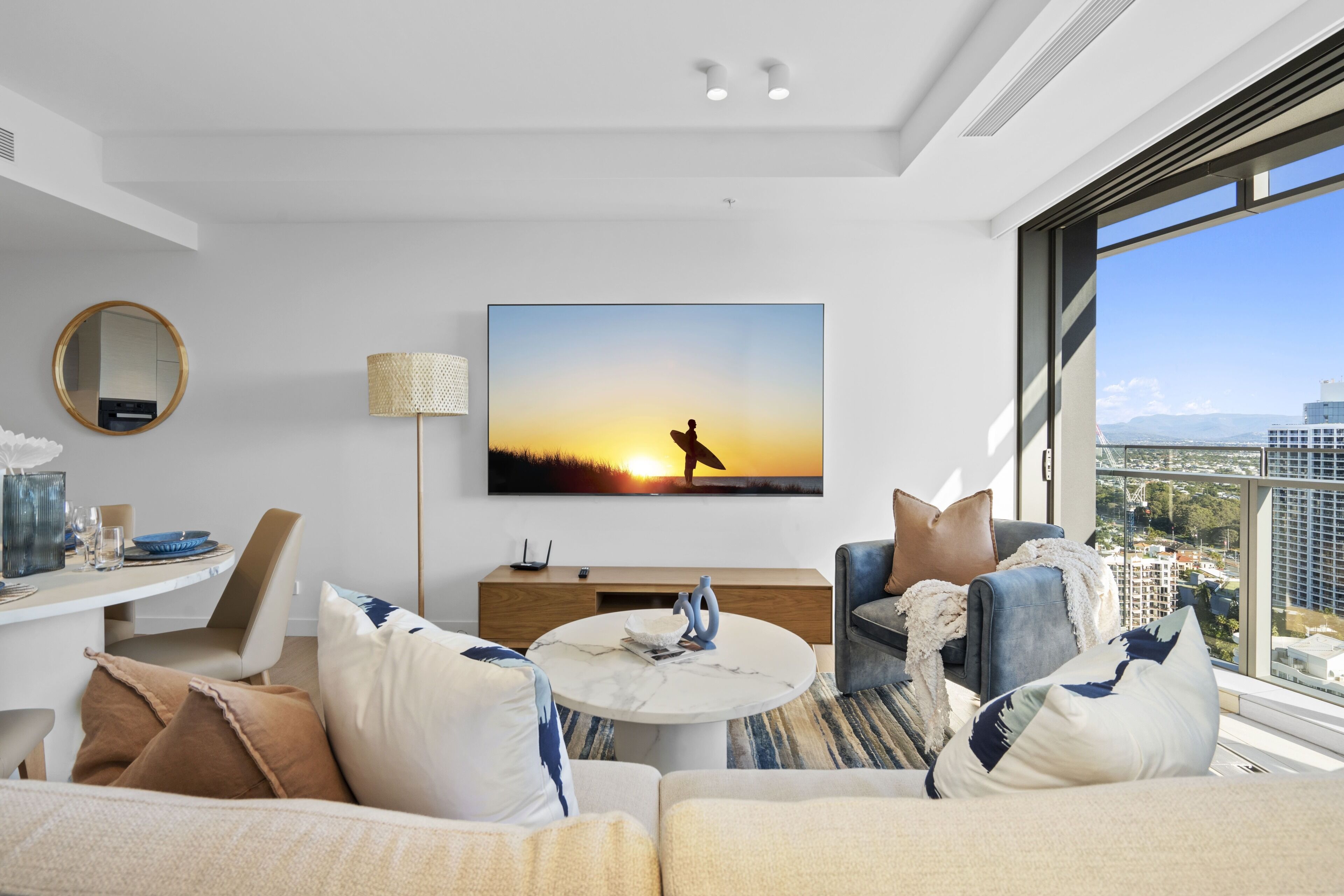 A modern living room with a large window, a flat-screen TV, and a dining area.