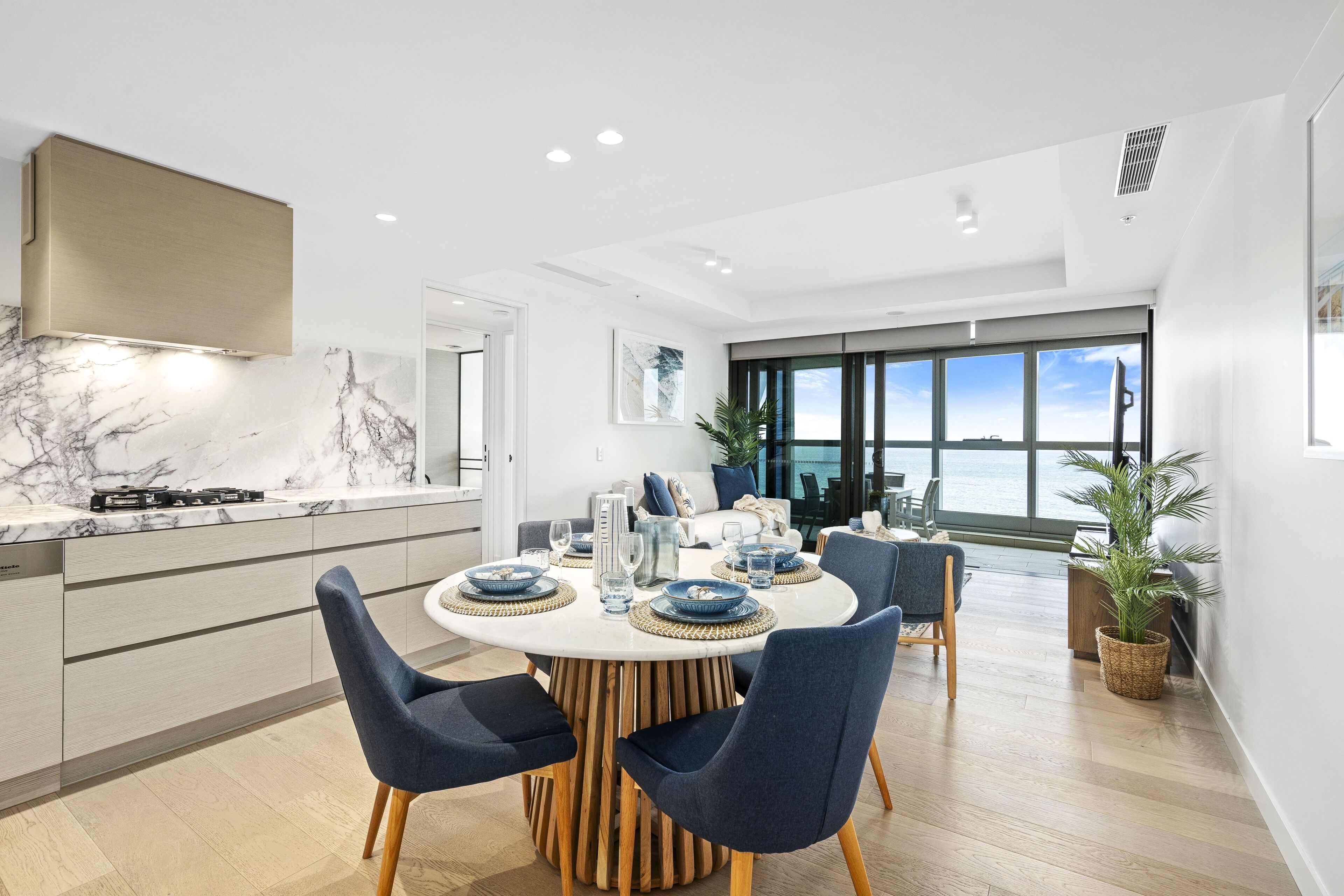 A modern kitchen with a marble countertop, a dining area with a round table and chairs, and a large window with a view.