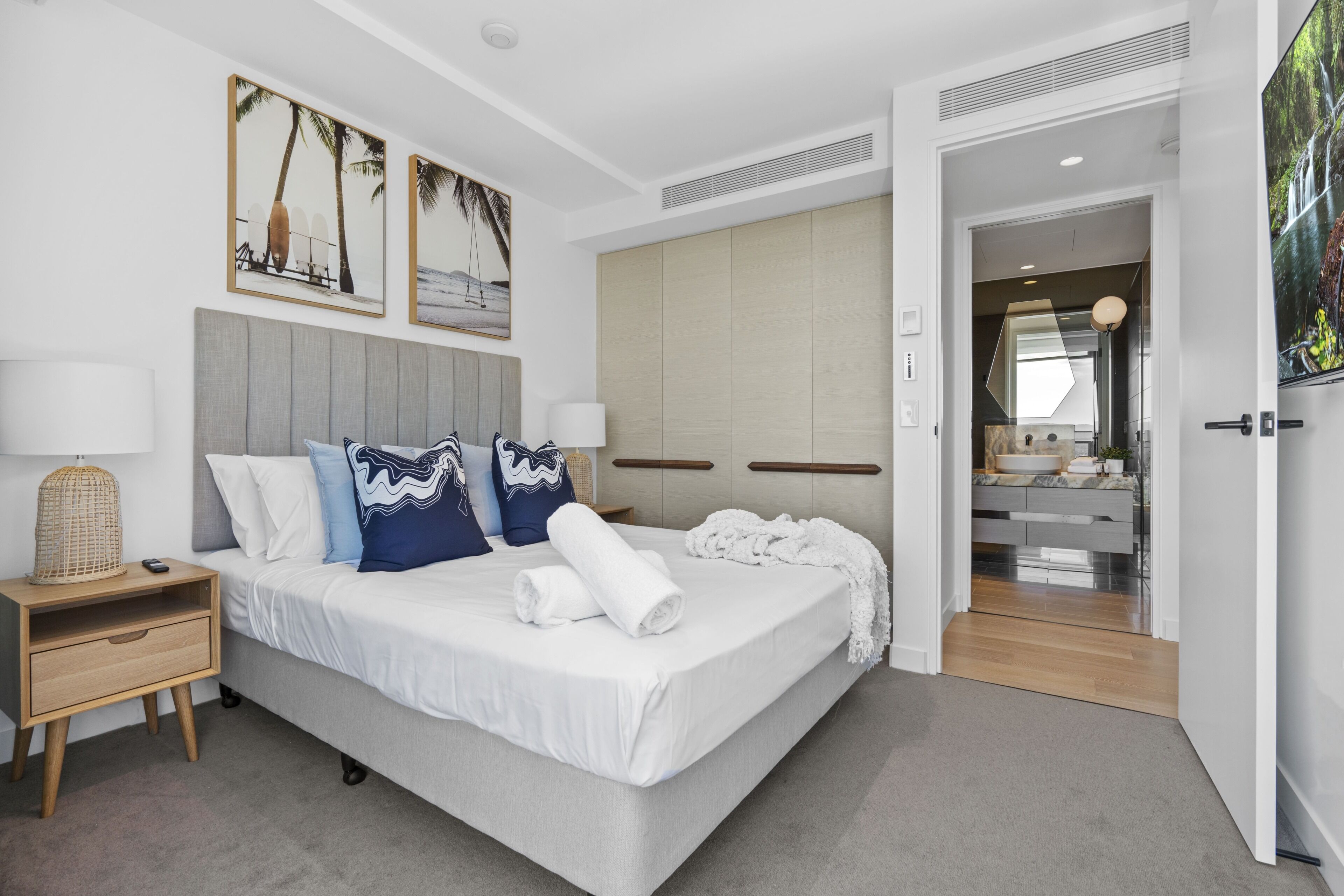 Camera d'albergo moderna con un letto grande, comodini, un armadio e un bagno visibile attraverso una porta aperta.