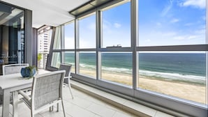 Un balcon avec vue sur l’océan, une table à manger avec des chaises et une grande fenêtre.