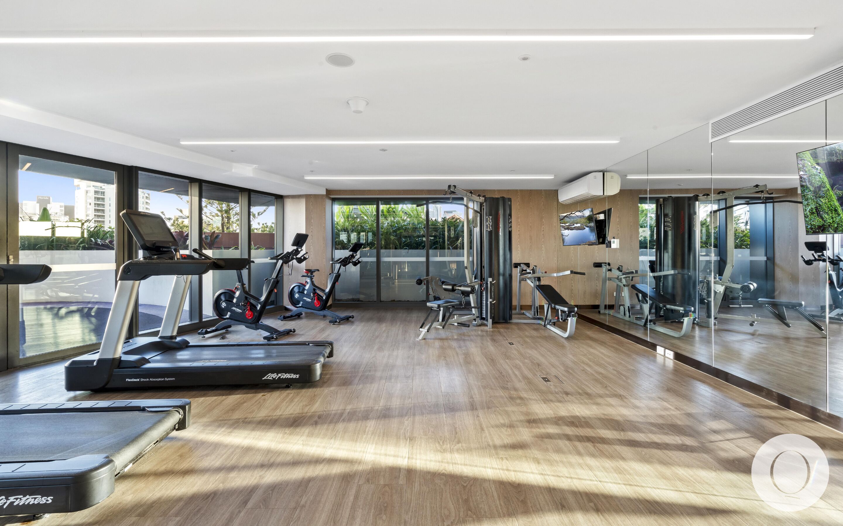 Ein modernes Fitnessstudio mit Laufbändern, Krafttrainingsgeräten und großen Fenstern mit Blick auf die Stadt.