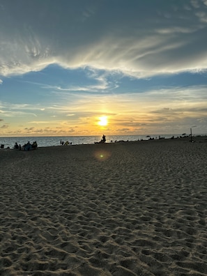 A beach with a sunset, people, and umbrellas.