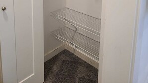 Un vestidor con puerta blanca, un estante de madera y estanterías metálicas.