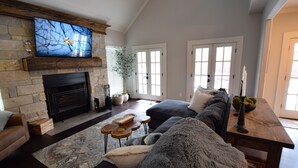 A spacious living room with a stone fireplace, a large flat-screen TV, a comfortable sofa, and a dining table with chairs. - Private place to hide away. Endless fun w/pool & game room for multiple families (Fort Worth)