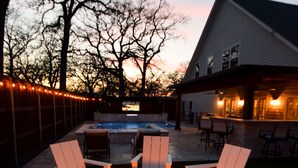 An outdoor patio with a fire pit surrounded by white chairs, a swimming pool, and a bar area with seating. - Private place to hide away. Endless fun w/pool & game room for multiple families (Fort Worth)
