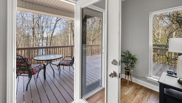 A room with a wooden deck, a sliding glass door, a small table, and a chair. - Lake Lanier Retreat + Deep Water Dock + Hot Tub (Gainesville)