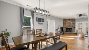A dining area with a wooden table and chairs, a bench, a potted plant, and a stone fireplace in the background. - Lake Lanier Retreat + Deep Water Dock + Hot Tub (Gainesville)