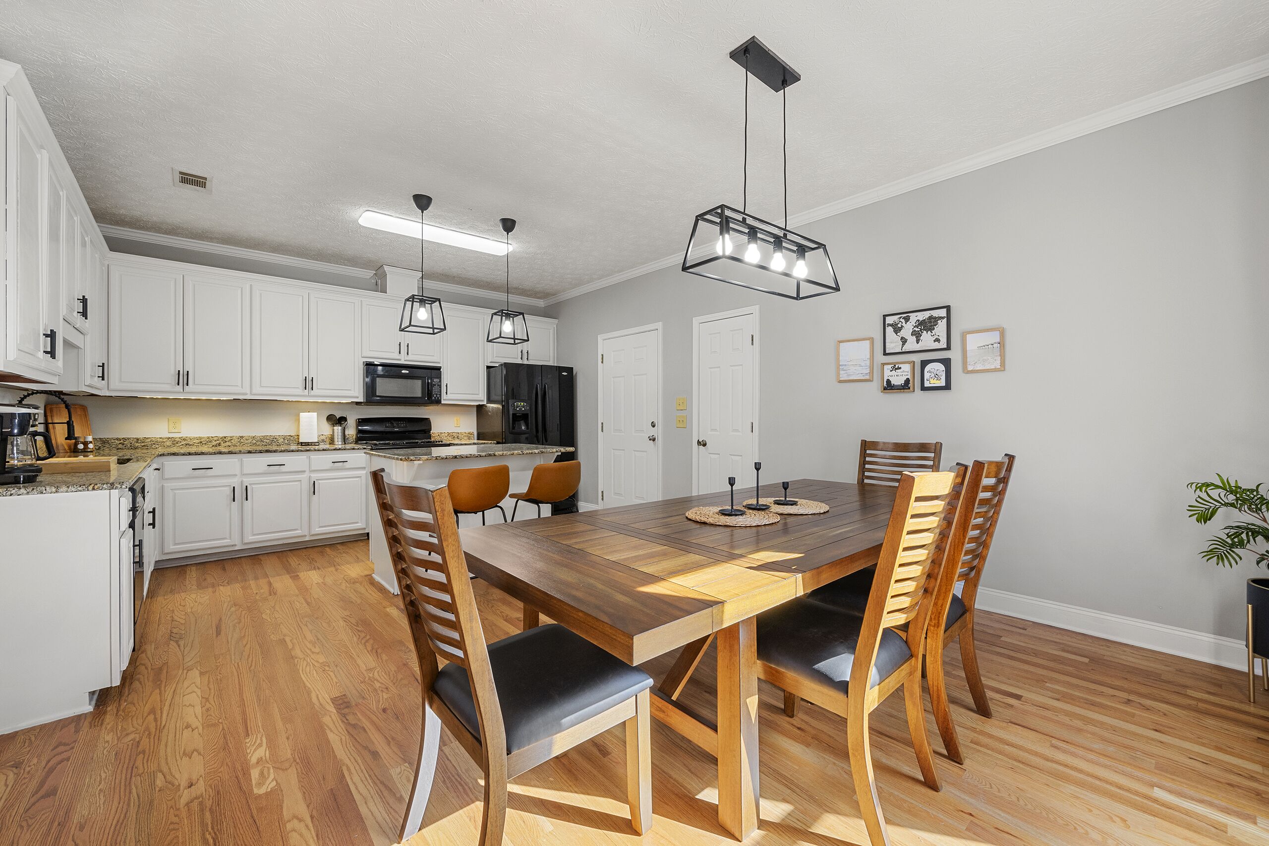 A modern kitchen with white cabinets, a wooden dining table, and a black refrigerator.