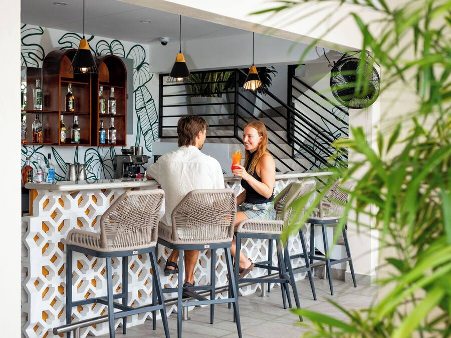 A bar area with wicker chairs, a bar counter, and shelves with bottles.