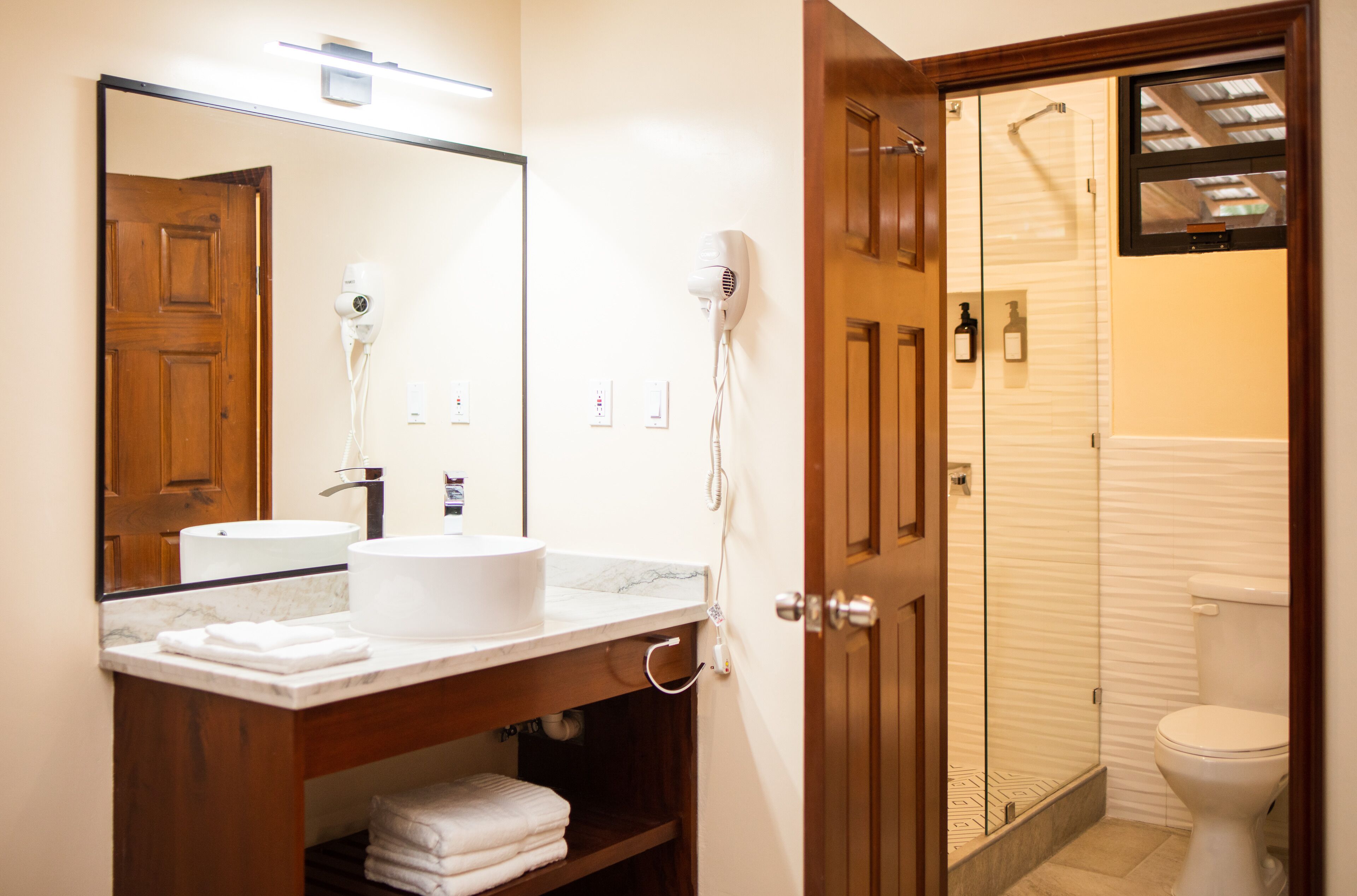 A bathroom with a wooden vanity, a white sink, a mirror, and a glass-enclosed shower.