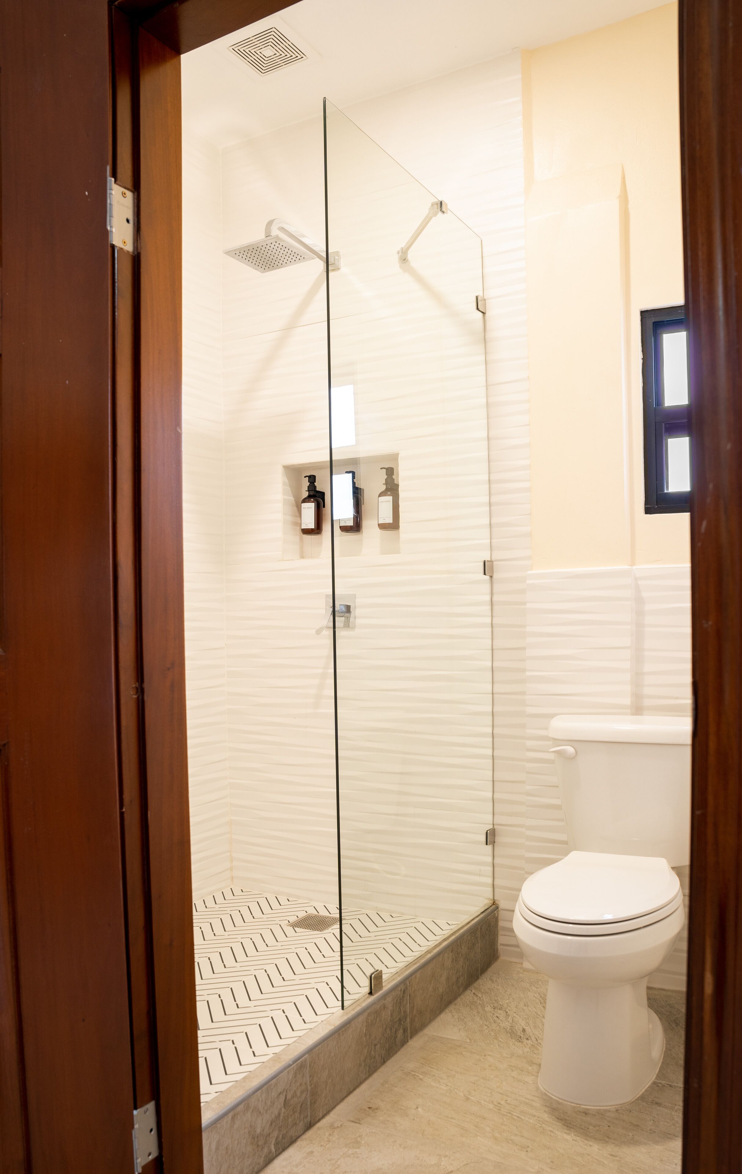 Et moderne badeværelse med en glasvæg omkring brusebadet, et hvidt toilet og et flisegulv.