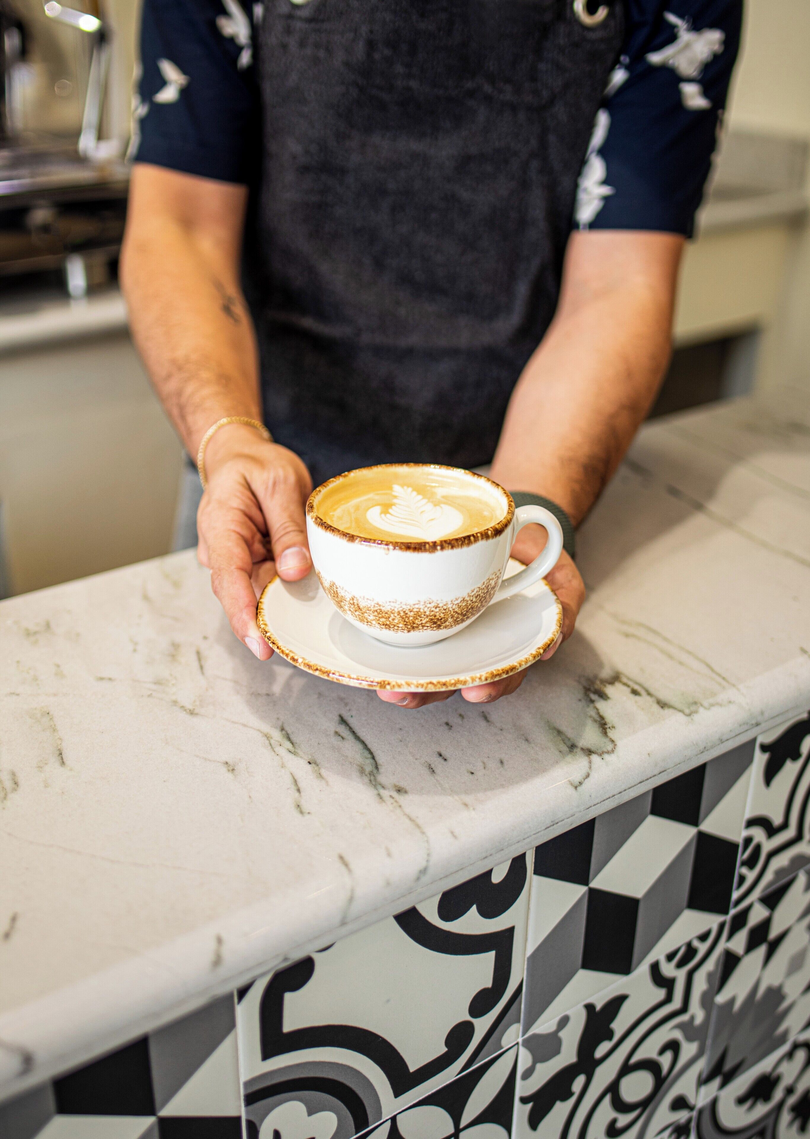 A person holding a cup of coffee with latte art on a marble countertop.