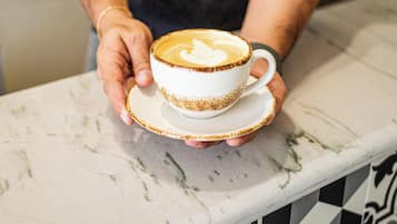 A person holding a cup of coffee with latte art on a marble countertop.