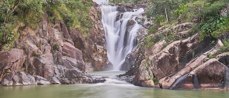 Uma cascata se derramando sobre terreno rochoso, cercada por vegetação exuberante.