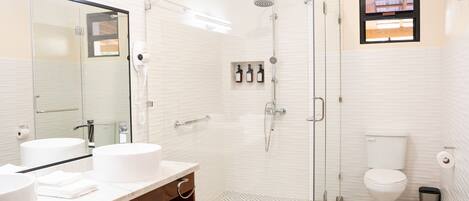Un baño moderno con ducha de vidrio, dos lavamanos, un inodoro y un espejo.
