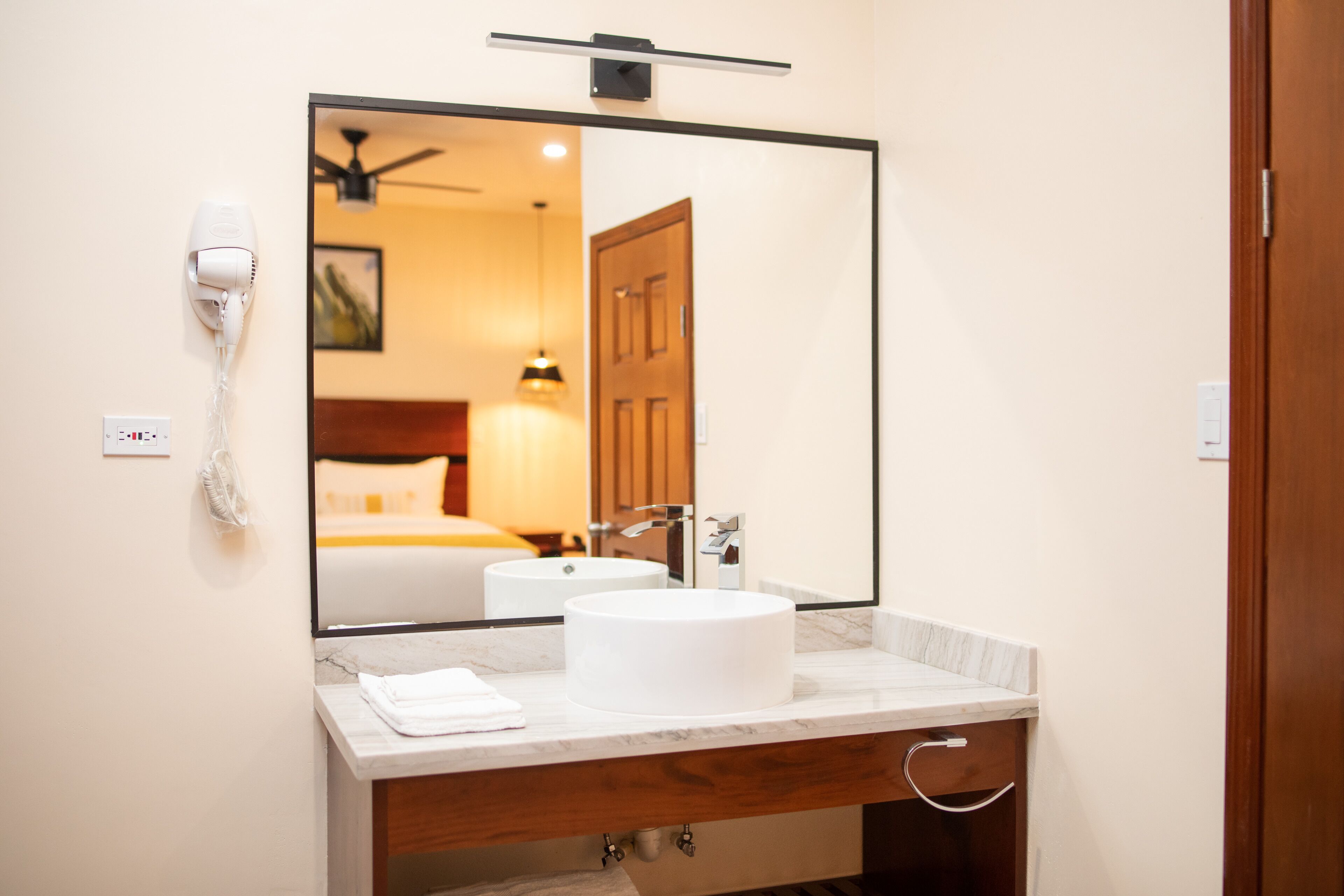 A hotel bathroom with a large mirror, a white sink, a towel, and a hairdryer on the wall.