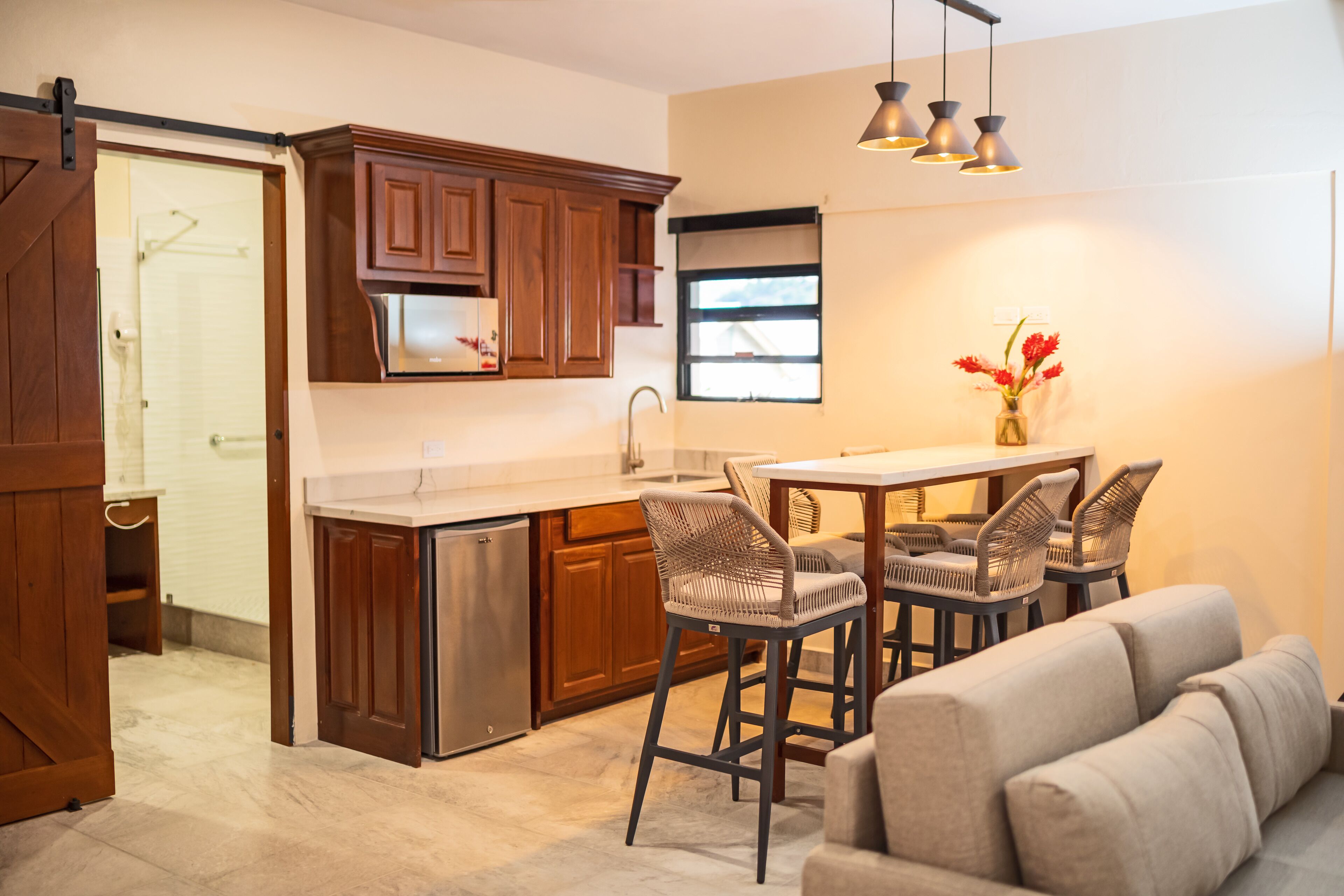 A modern kitchen with wooden cabinets, a stainless steel refrigerator, and a dining area with bar stools.