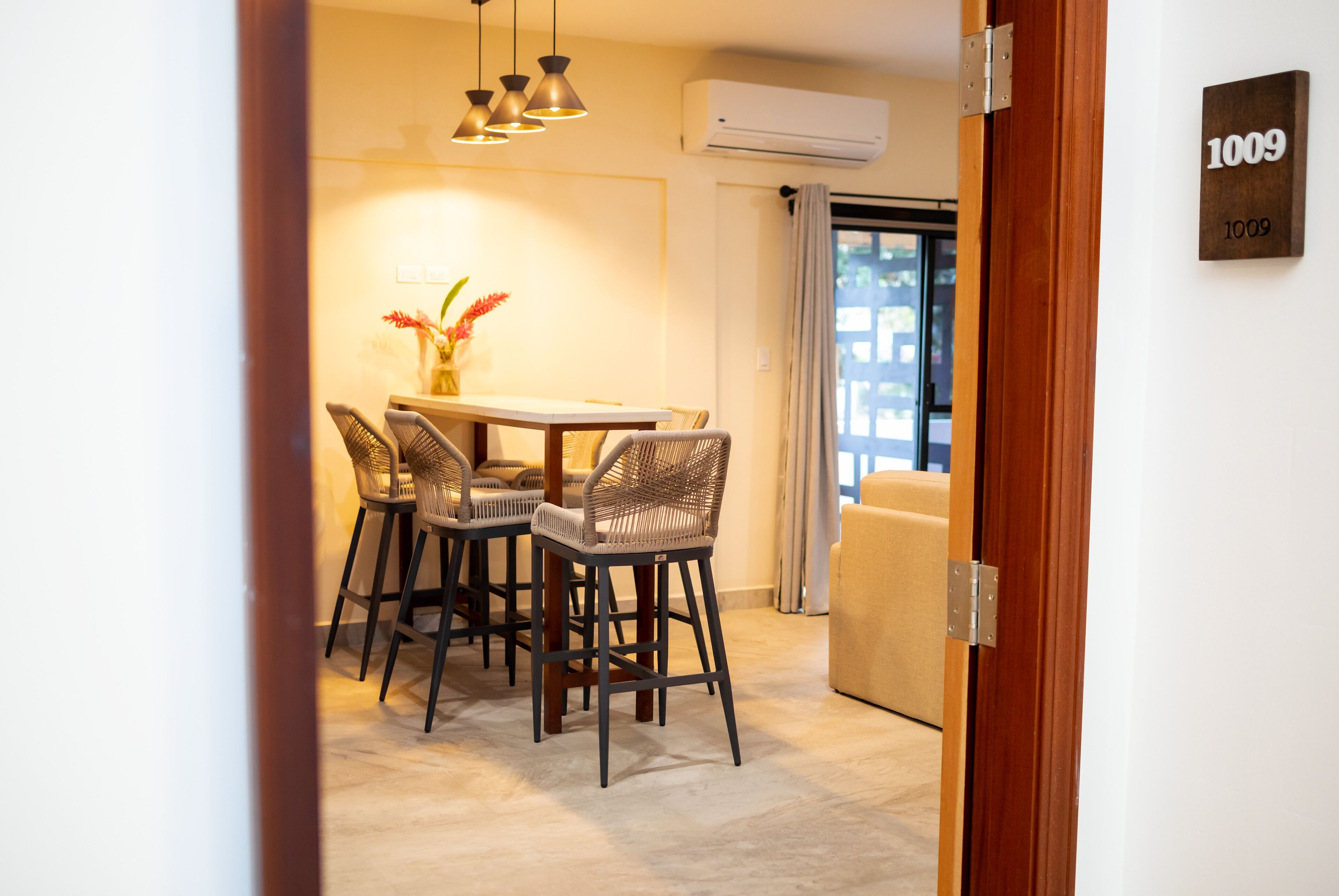 A dining area with a table and four chairs, an air conditioning unit, and a door with a number sign.