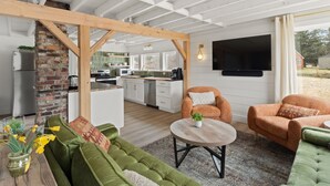 Et moderne køkken med hvide skabe, en murstensvæg og et træloft. Der er et spiseområde med grønne sofaer og et rundt bord.