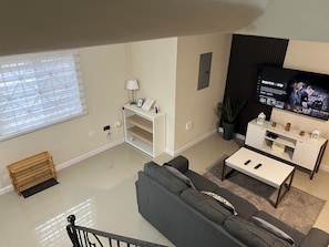 Una sala de estar moderna con un sofá gris, una mesa de centro blanca, un televisor en la pared y una mesita auxiliar blanca.