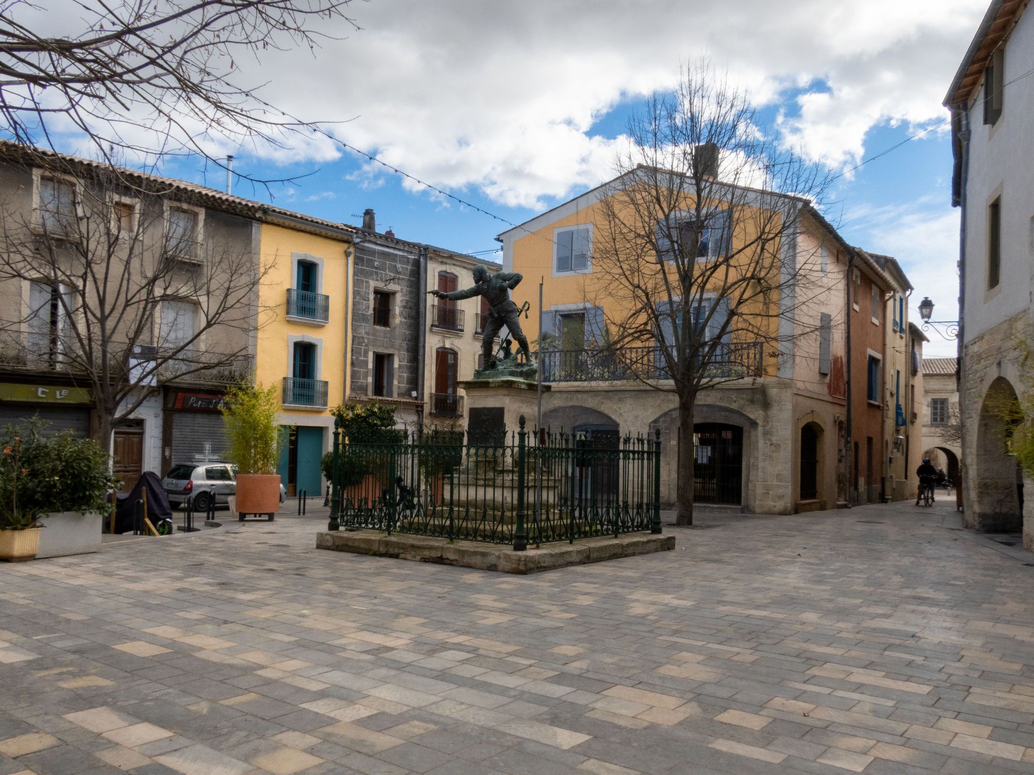 A courtyard with a statue, buildings with balconies, and a paved ground.