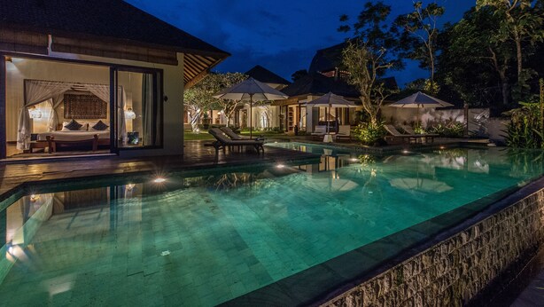 A nighttime view of a resort with a swimming pool, lounge chairs, and umbrellas. - Luxury tropical 5-bedroom villa, five minutes to the beach - Canggu (Bali)