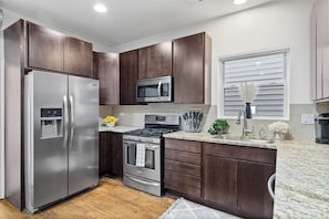 Una cocina moderna con electrodomésticos de acero inoxidable, armarios de madera oscura y encimera de granito.