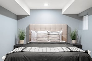Un dormitorio moderno con un cabecero capitonado, dos mesitas de noche con plantas en macetas y una cama grande con ropa de cama a rayas.