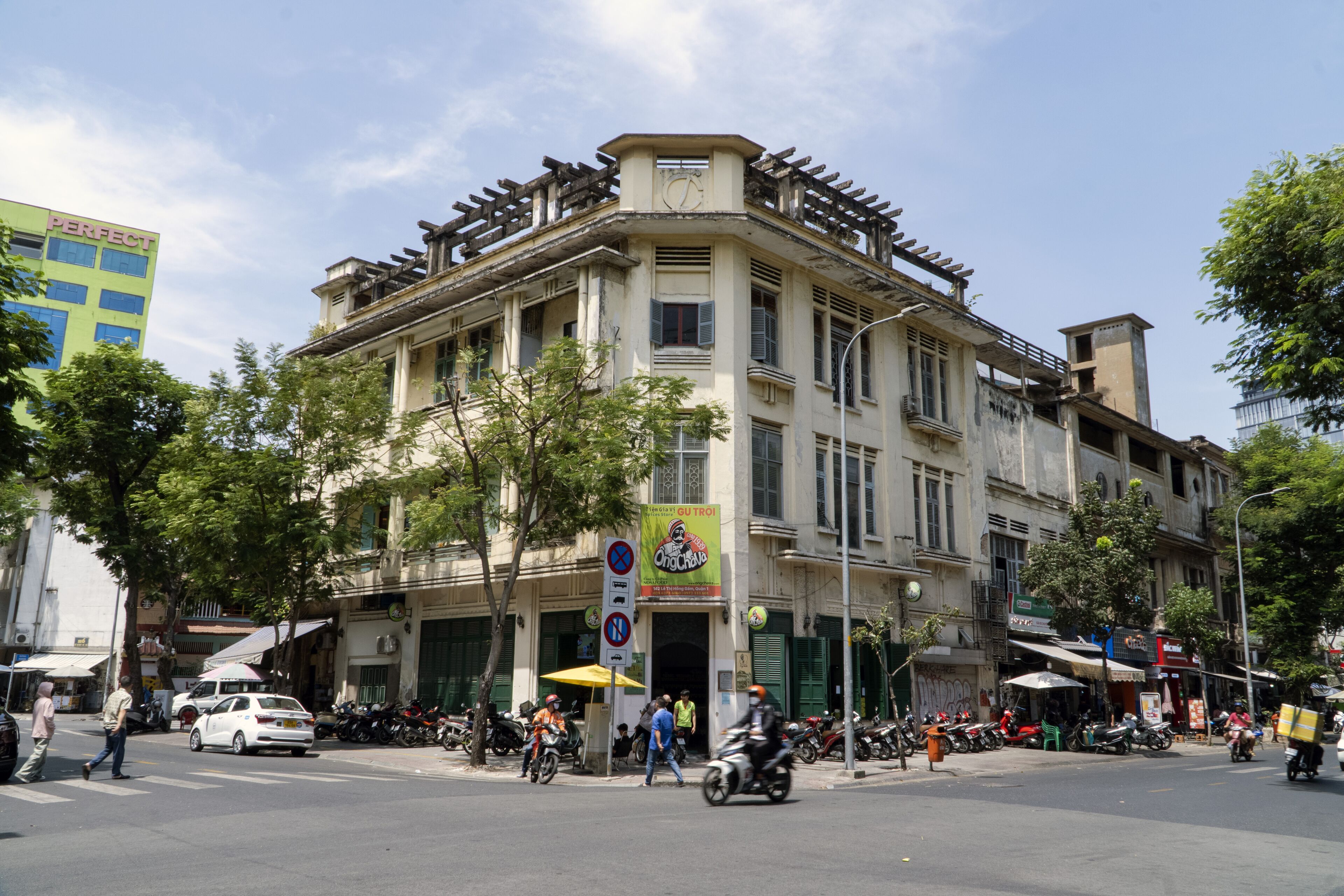 A multi-story building with a corner entrance, a signboard, and a street view with pedestrians and vehicles.