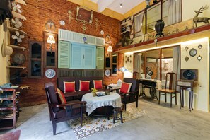 Una habitación con pared de ladrillo, un conjunto de sofá, una mesa con mantel de encaje y un ventilador de techo.