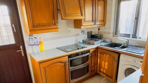 A kitchen with wooden cabinets, a stove, oven, and a washing machine. - 1 Bed House - Parking & Wifi (Birmingham)