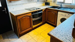 A kitchen with wooden cabinets, a built-in oven, a microwave, and a washing machine. - 1 Bed House - Parking & Wifi (Birmingham)