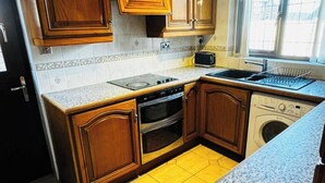 A compact kitchen with wooden cabinets, a built-in oven, a microwave, a sink, and a washing machine. - 1 Bed House - Parking & Wifi (Birmingham)