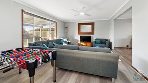A spacious living area with a foosball table, grey sofas, a television, and a ceiling fan. - Sea Breeze A cosy 4/1 holiday home, just 300m from Lancelin Back Beach (Lancelin)