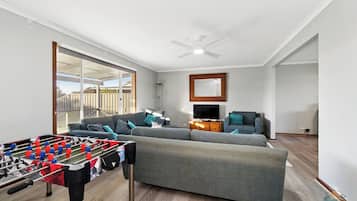 A spacious living area with a foosball table, grey sofas, a television, and a ceiling fan.