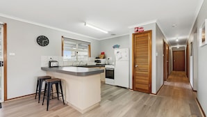 A kitchen with a central island, a microwave, a toaster, and a refrigerator. There is a clock on the wall and a wooden door with a 'Welcome' sign. - Sea Breeze A cosy 4/1 holiday home, just 300m from Lancelin Back Beach (Lancelin)