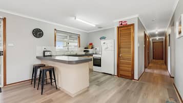 A kitchen with a central island, a microwave, a toaster, and a refrigerator. There is a clock on the wall and a wooden door with a 'Welcome' sign.