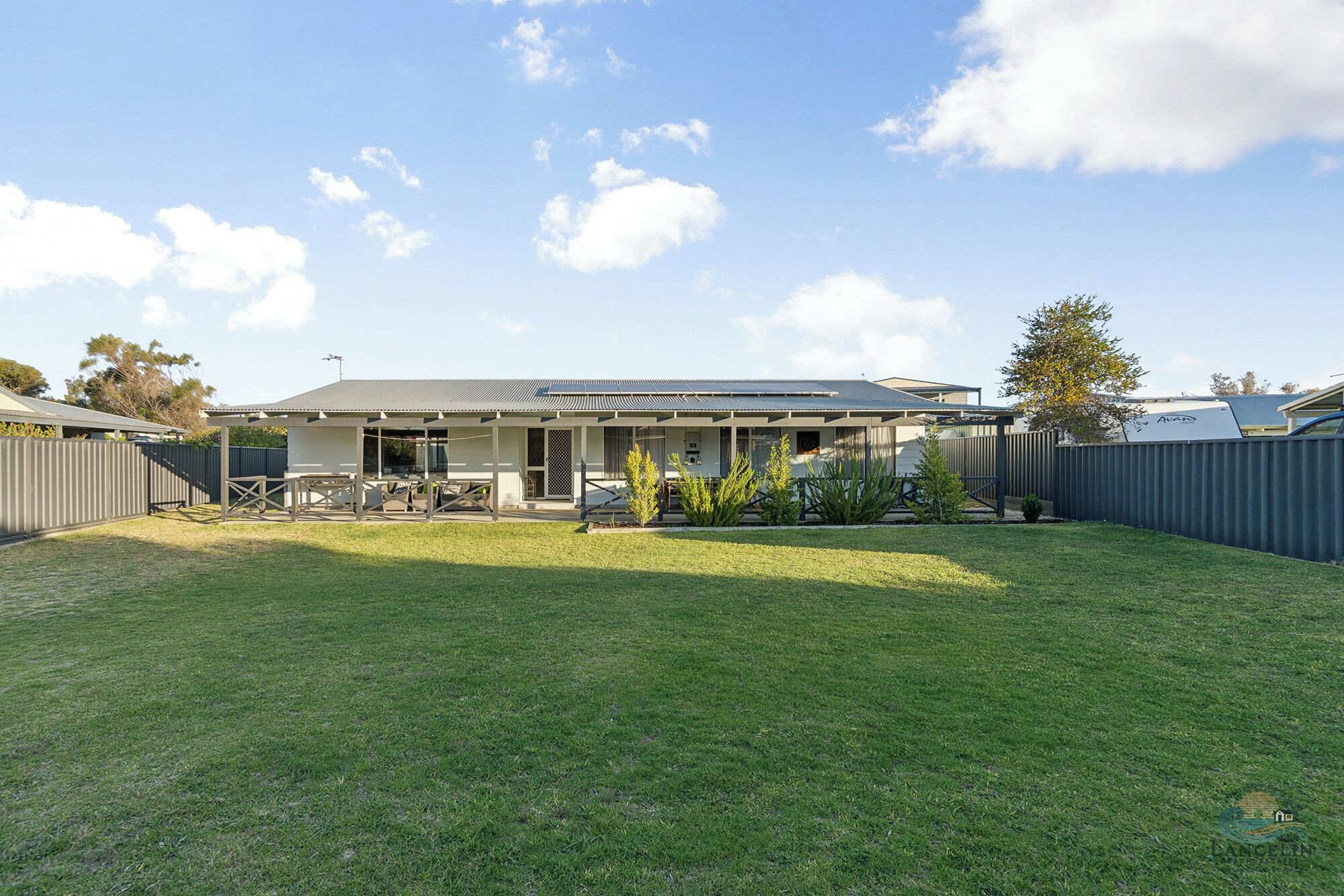 A residential house with a covered patio, a fenced backyard, and a well-maintained lawn.