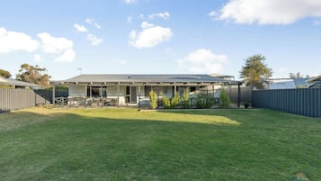 A residential house with a covered patio, a fenced backyard, and a well-maintained lawn.
